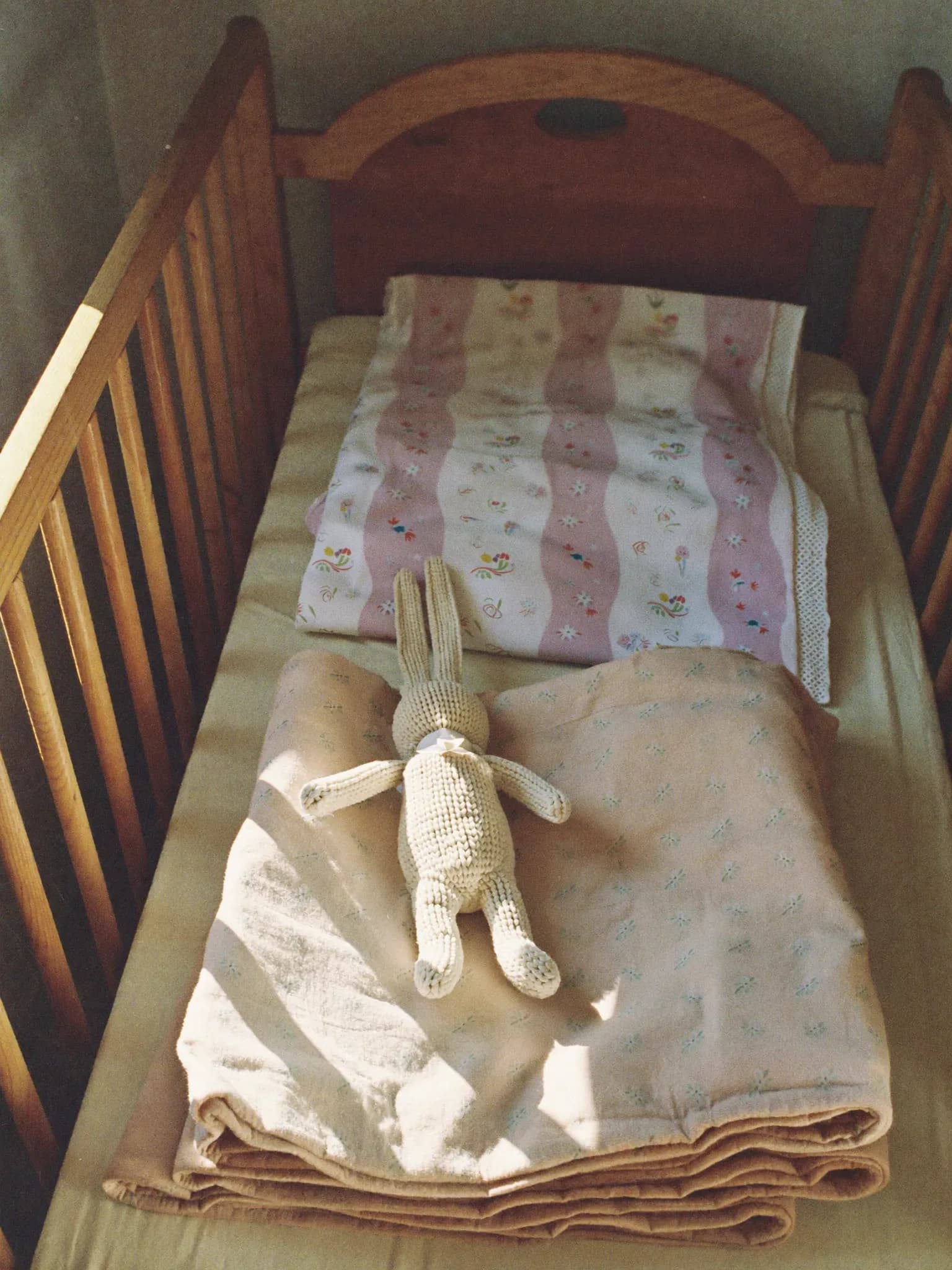 KI-generiert: Sonniges Kinderzimmer mit Holzbett, gefalteten Mulltüchern und einem Strickhasen.
