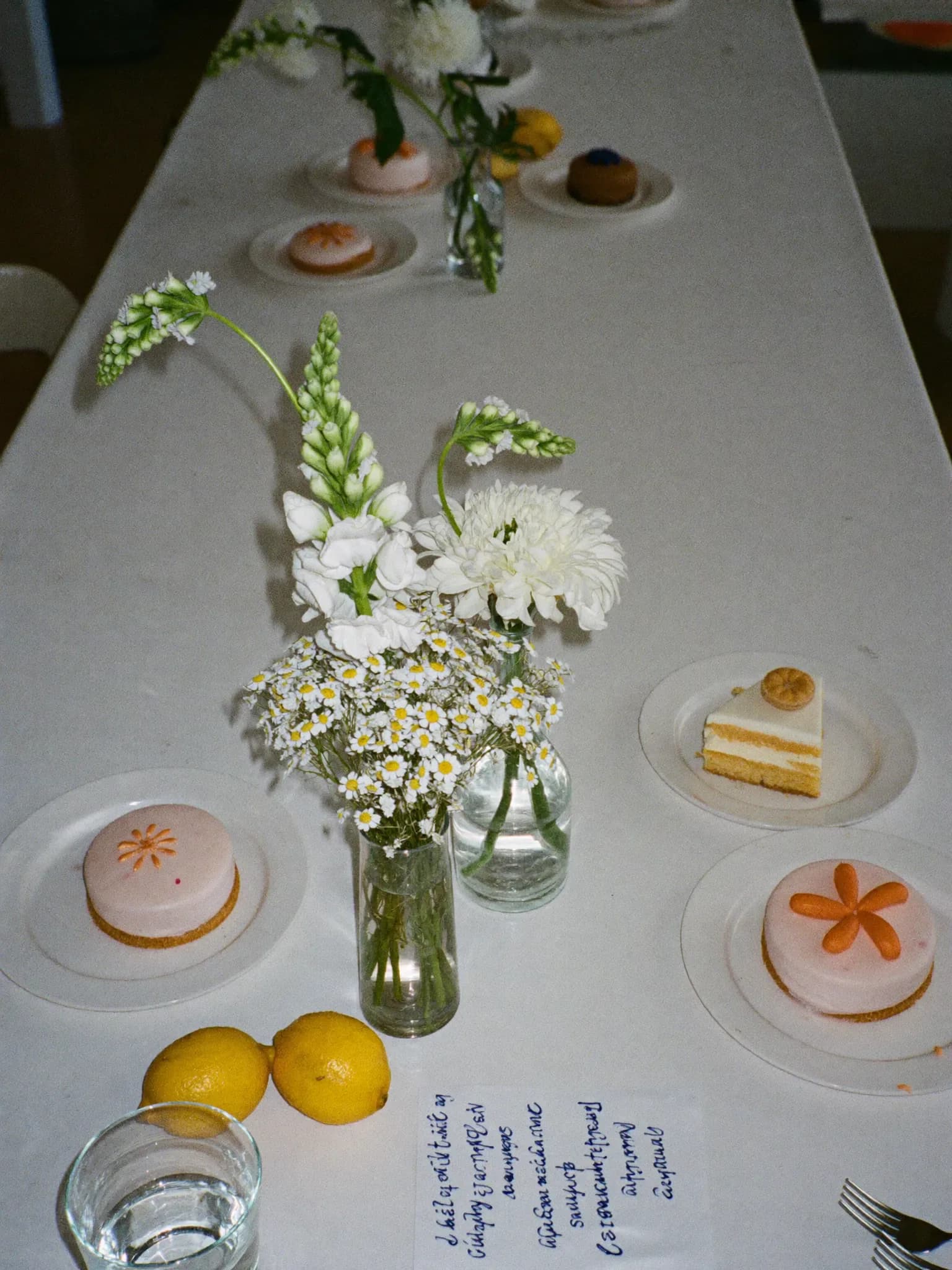 KI-generiert: Babyparty-Tisch mit weißen Blumen, Limonade, kleinen Törtchen und Platzkarte.