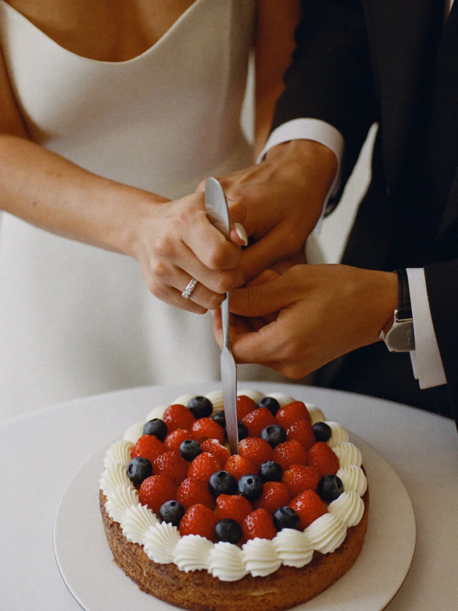 Generata con IA: due mani tagliano insieme una torta ai frutti di bosco.