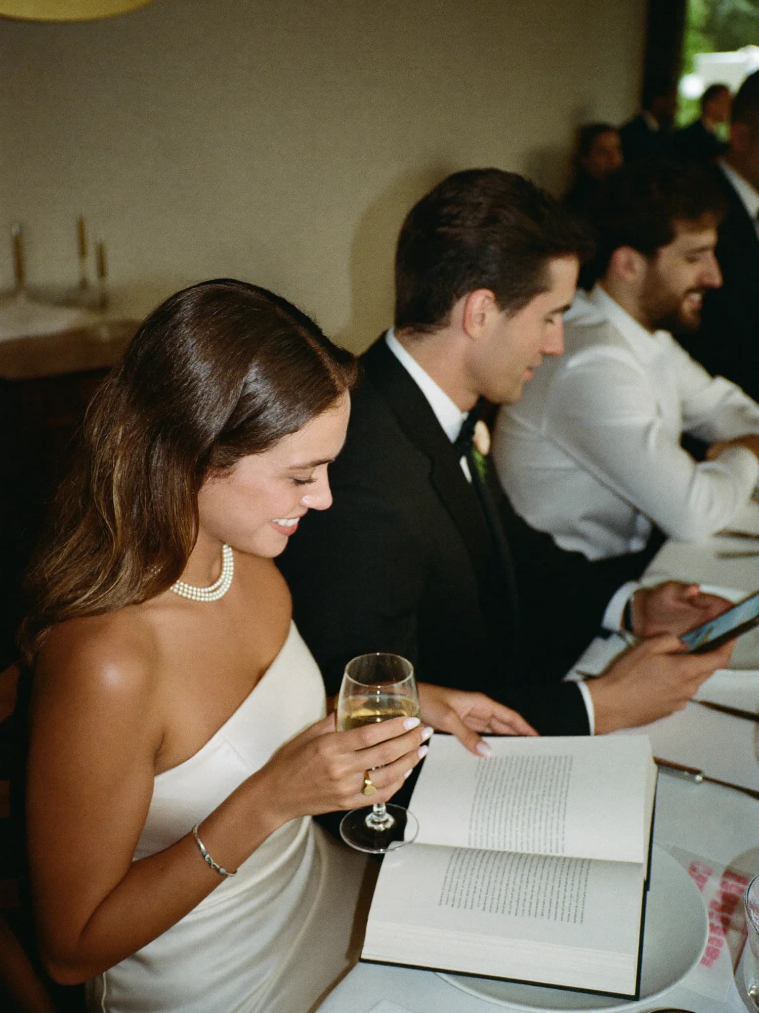Generata con IA: due invitati al matrimonio a tavola, una donna legge sorridendo sul telefono di un uomo.