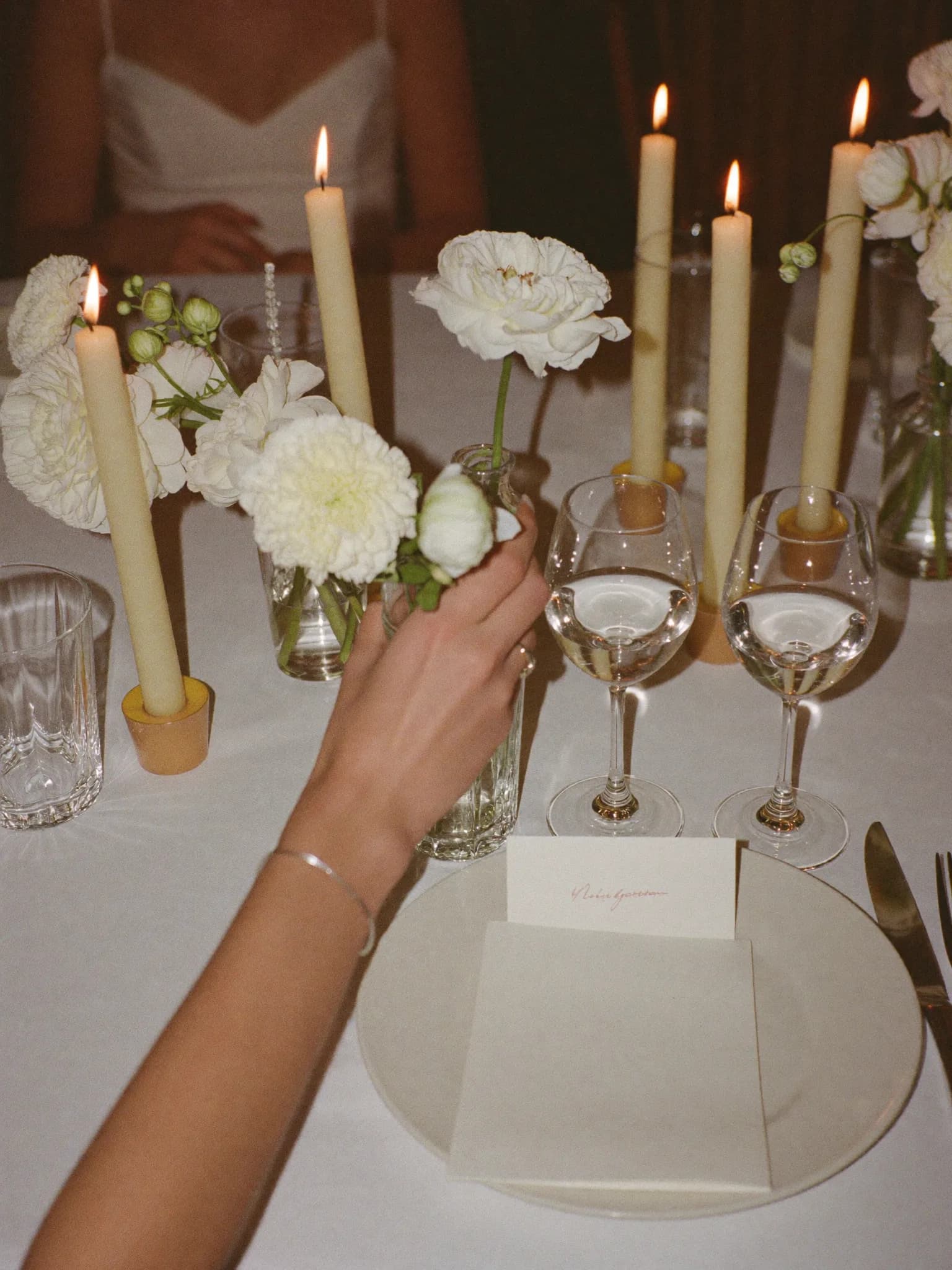 Generata con IA: una tavola apparecchiata a festa con candele, fiori bianchi, bicchieri e segnaposto.
