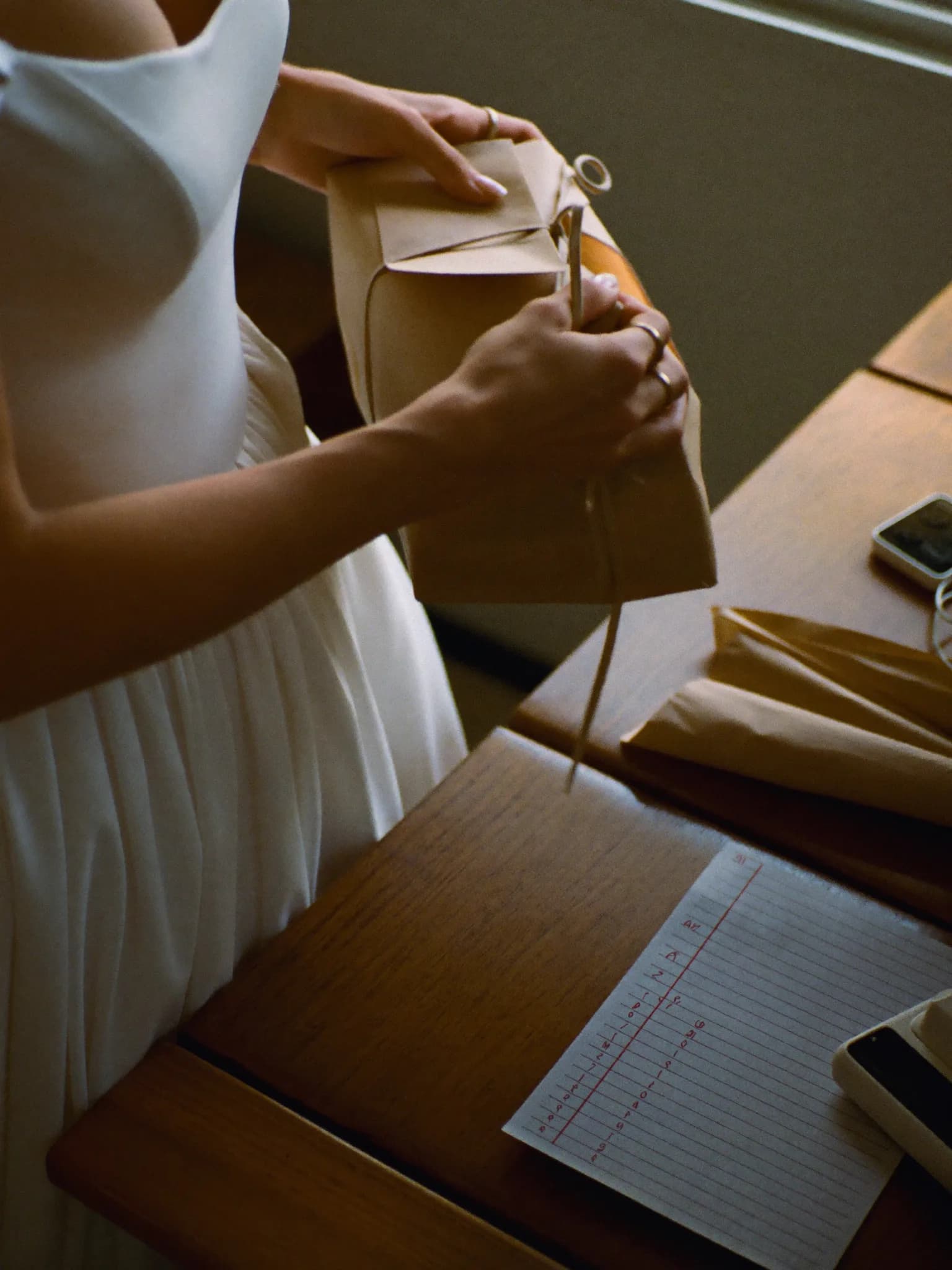Generata con IA: una sposa apre un regalo in carta da pacco, accanto un telefono con una lista.