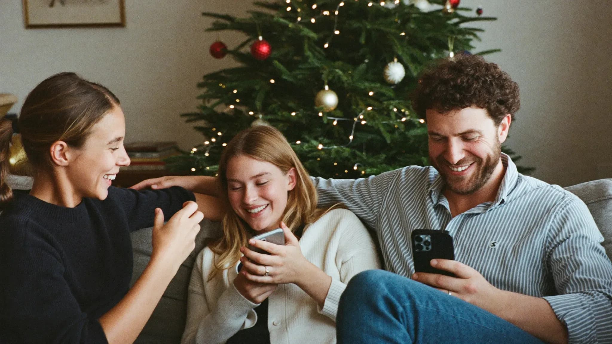 AI-genereret: En familie griner på sofaen foran juletræet over en mobil.