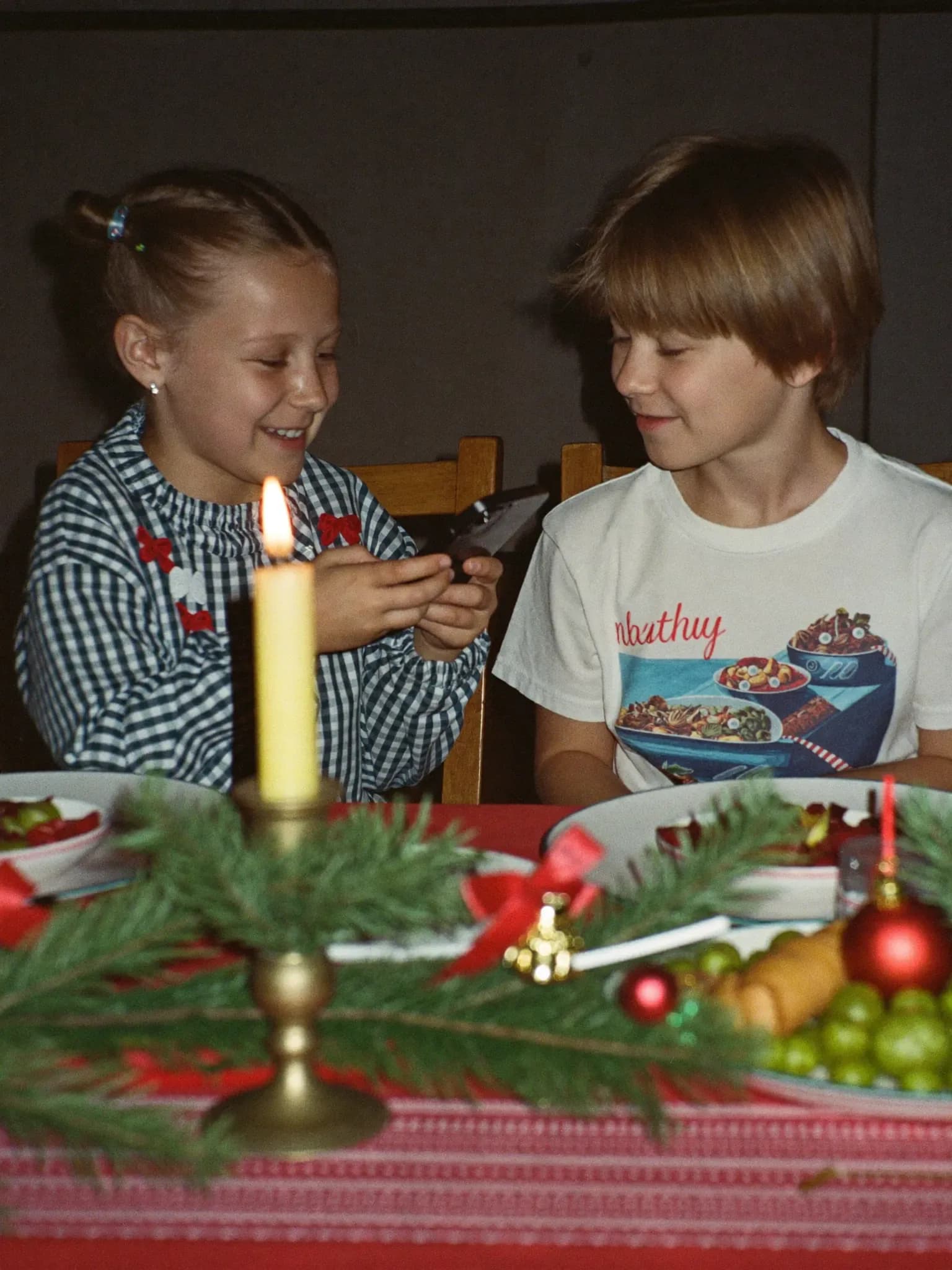 AI-genereret: To søskende ved julebordet, den ene viser den anden noget på mobilen.
